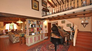 A spacious living room with a grand piano, a large bookshelf, and a staircase leading to an upper level. - Villa San Savino (Monte San Savino)