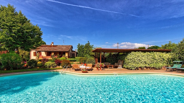 A swimming pool with lounge chairs and a gazebo, surrounded by lush greenery and a house. - Villa San Savino (Monte San Savino)