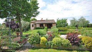 A house with a tiled roof, surrounded by a well-maintained garden with various plants and a lawn. - Villa San Savino (Monte San Savino)