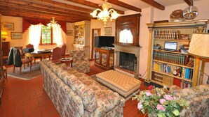 A traditional living room with a fireplace, wooden beams, a chandelier, and a bookshelf. - Villa San Savino (Monte San Savino)