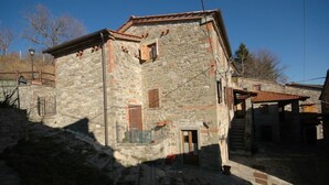 A stone building with a wooden door, a small window, and a staircase leading to an upper level. - Annarita (Pratovecchio Stia)