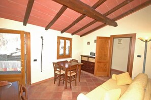 Un comedor con mesa y sillas de madera, un sofá y una televisión en la zona de la cocina.