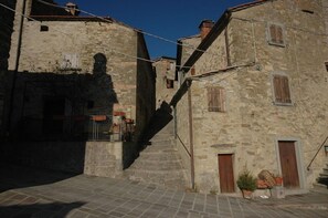 Una estrecha calle empedrada flanqueada por edificios antiguos con contraventanas de madera y una pequeña escalera que sube a un nivel superior.