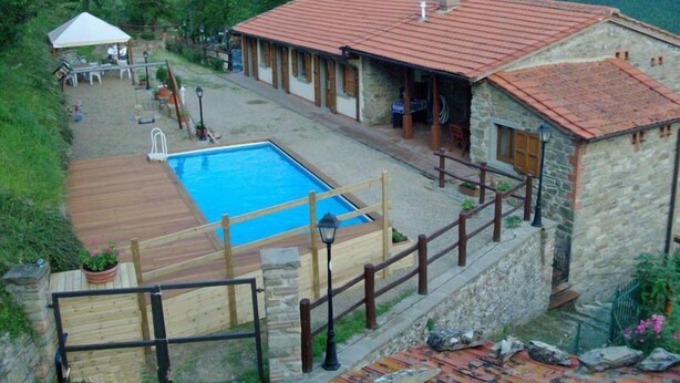 A stone building with a red-tiled roof, a swimming pool, and a wooden deck. - Annarita (Pratovecchio Stia)