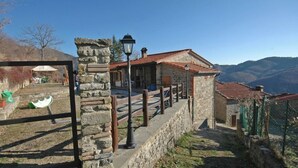 A stone building with a red-tiled roof, a stone wall, and a metal gate. - Annarita (Pratovecchio Stia)