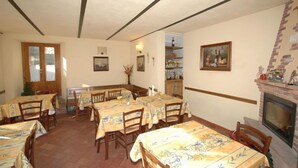 A dining area with multiple tables and chairs, a fireplace, and a window with blinds. - Annarita (Pratovecchio Stia)