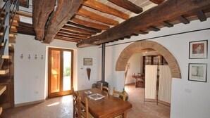 A dining area with a wooden table and chairs, a staircase with wooden beams, and an arched doorway leading to another room. - Poggio Del Sole (Cortona)