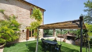 A stone building with a covered patio area featuring a table and chairs. - Poggio Del Sole (Cortona)