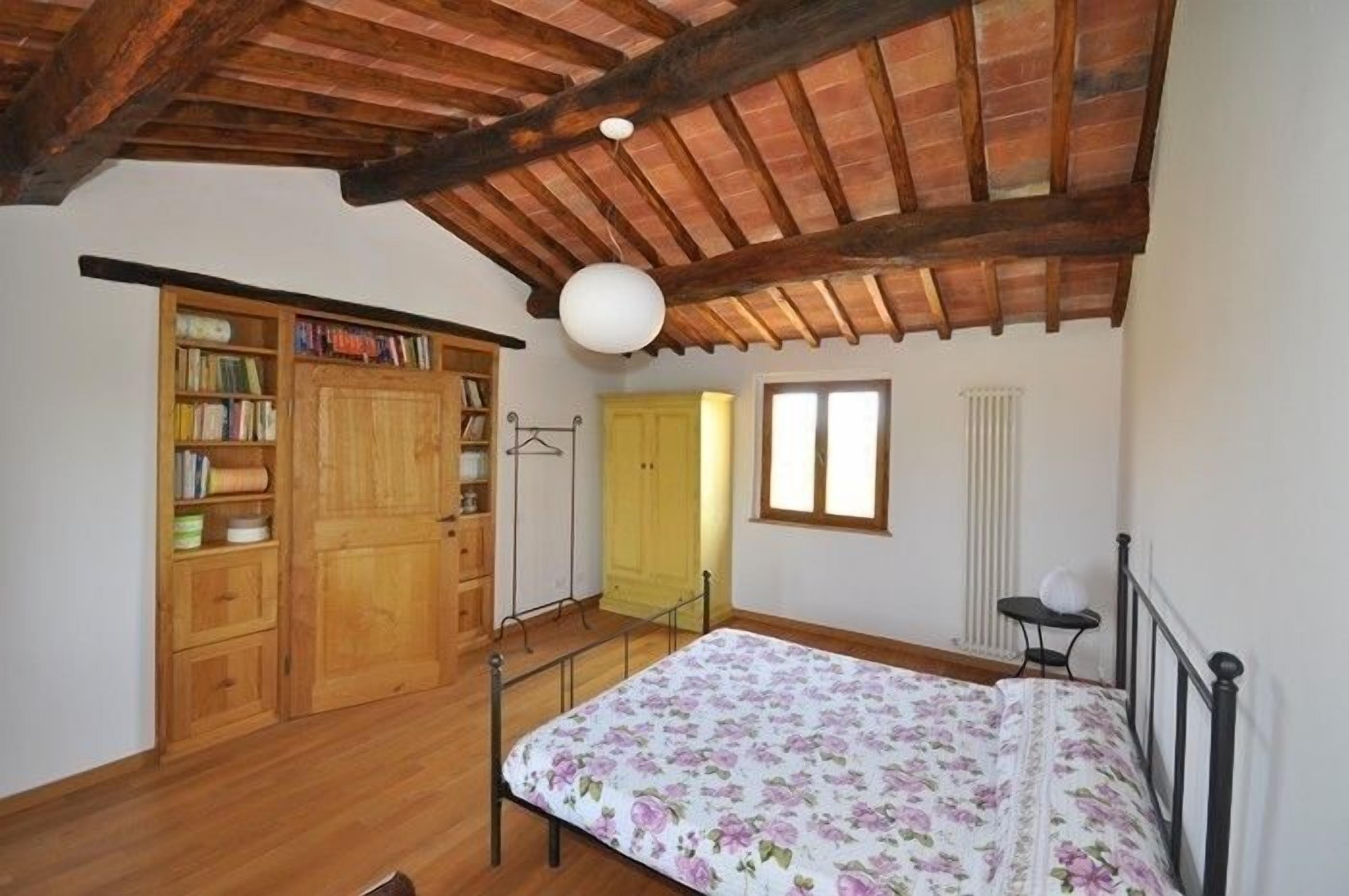 A bedroom with wooden furniture, a bed with a floral bedspread, a wardrobe, and a radiator.