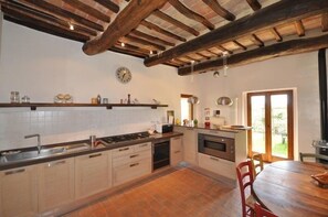 A kitchen with white cabinets, a wooden ceiling, and a dining area with a table and chairs. - Poggio Del Sole (Cortona)