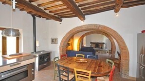 A dining area with a wooden table and chairs, a kitchen with modern appliances, and a rustic brick archway. - Poggio Del Sole (Cortona)