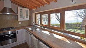 A kitchen with wooden cabinets, a stove, and a large window with a view of trees and mountains. - Gellino (Arezzo)