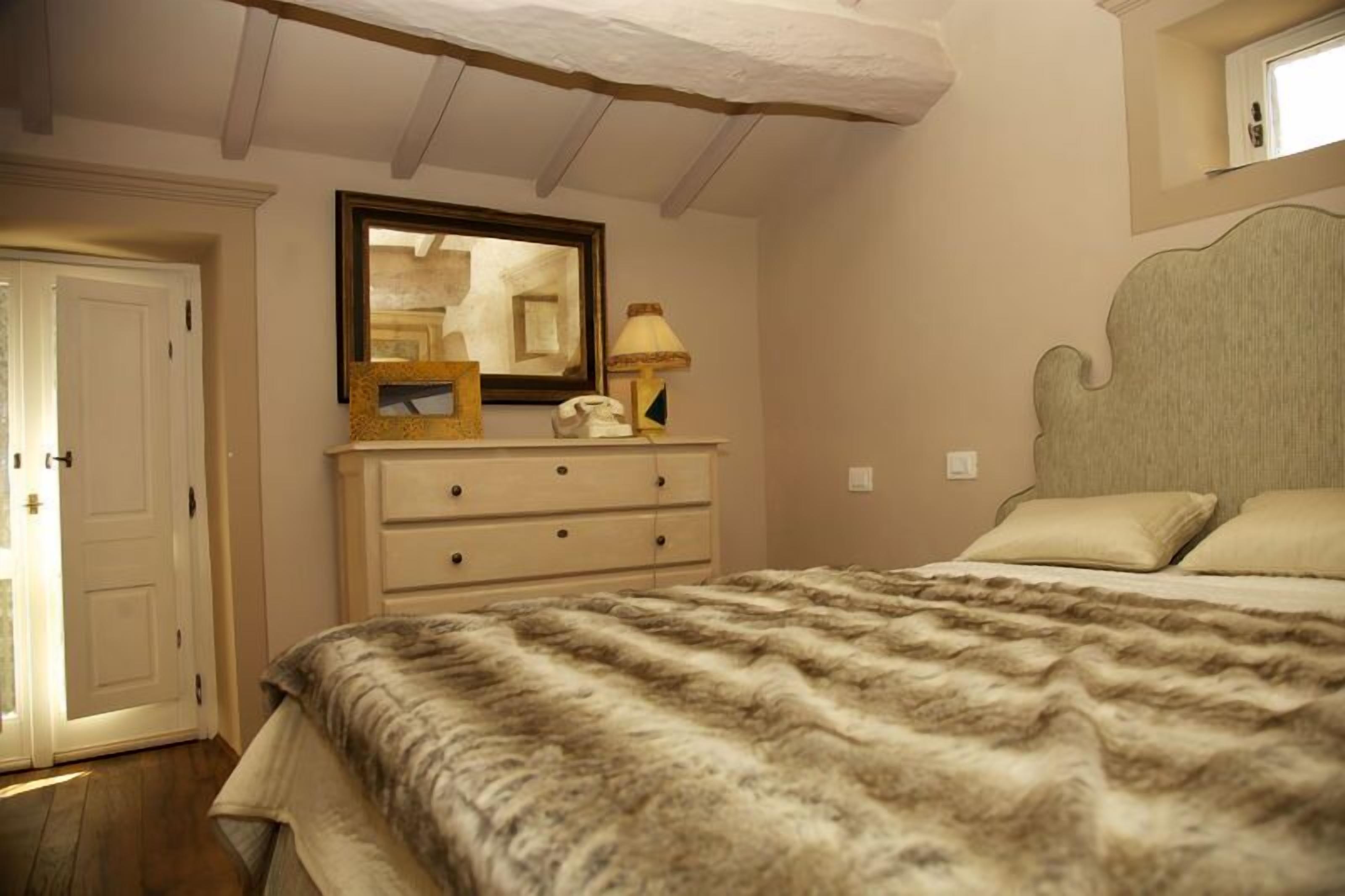 A bedroom with a bed, a dresser, a mirror, and a lamp.