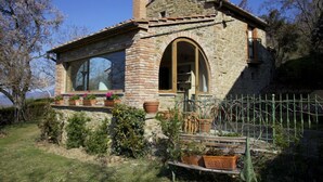 A stone house with a large arched window, a small porch with potted plants, and a metal fence. - Gellino (Arezzo)