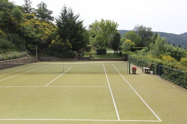 An outdoor tennis court with a net, surrounded by trees and a stone wall. - Gellino (Arezzo)