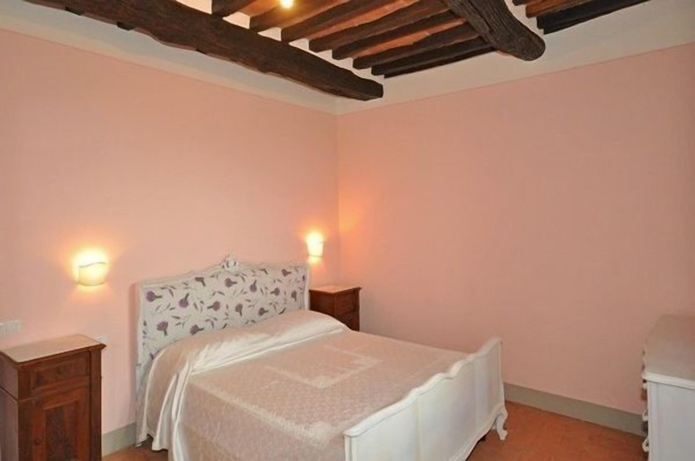 Een slaapkamer met een bed, twee nachtkastjes en een plafond met zichtbare balken.