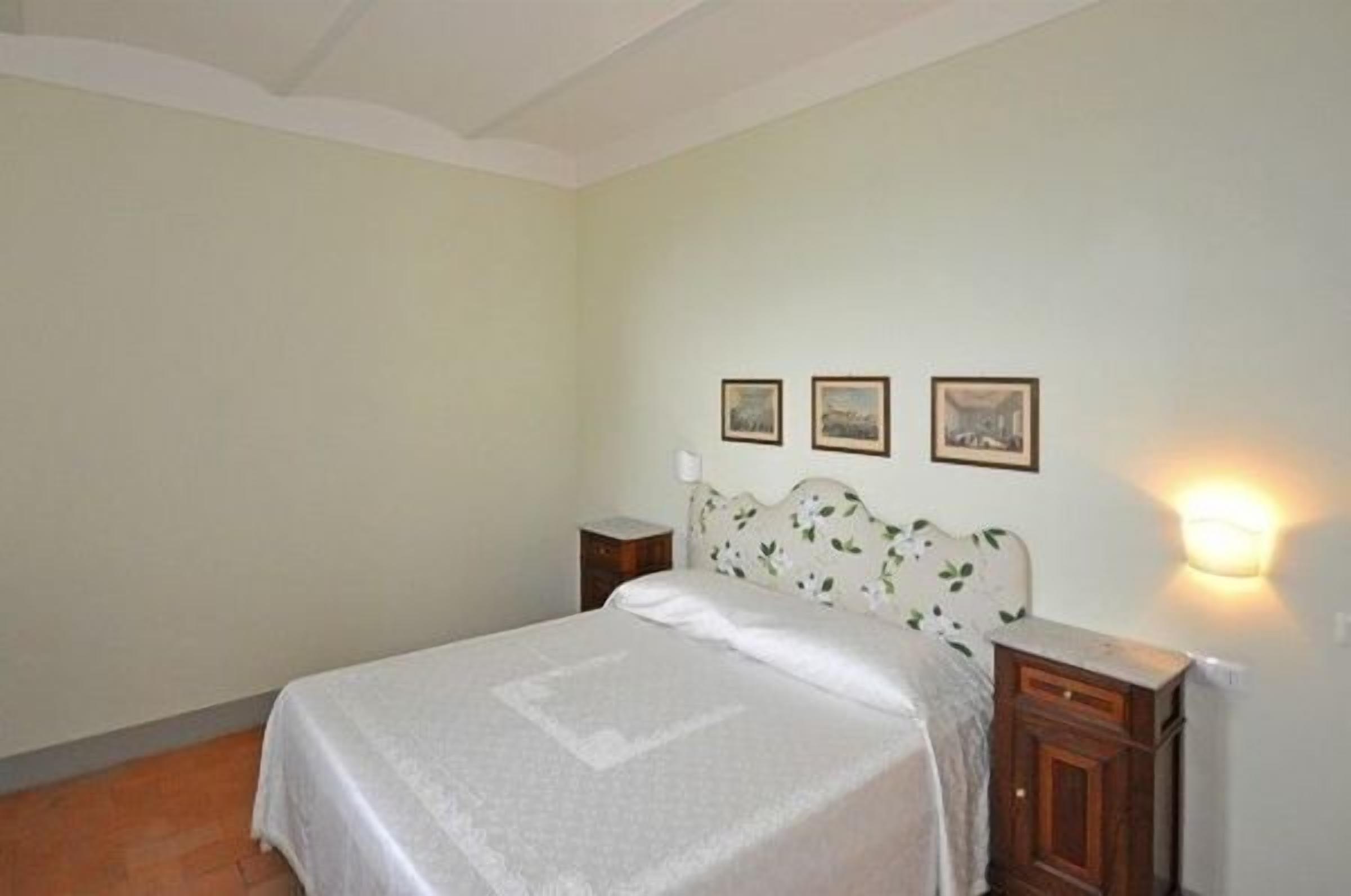 Une chambre à coucher comprenant un lit, une table de chevet, une lampe fixée au mur et trois tableaux encadrés accrochés au mur.