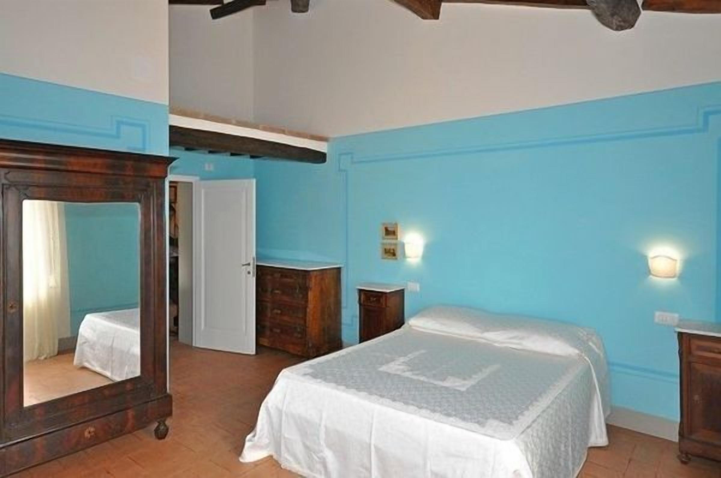 A bedroom with a bed, a dresser, a mirror, and two wall-mounted lights.