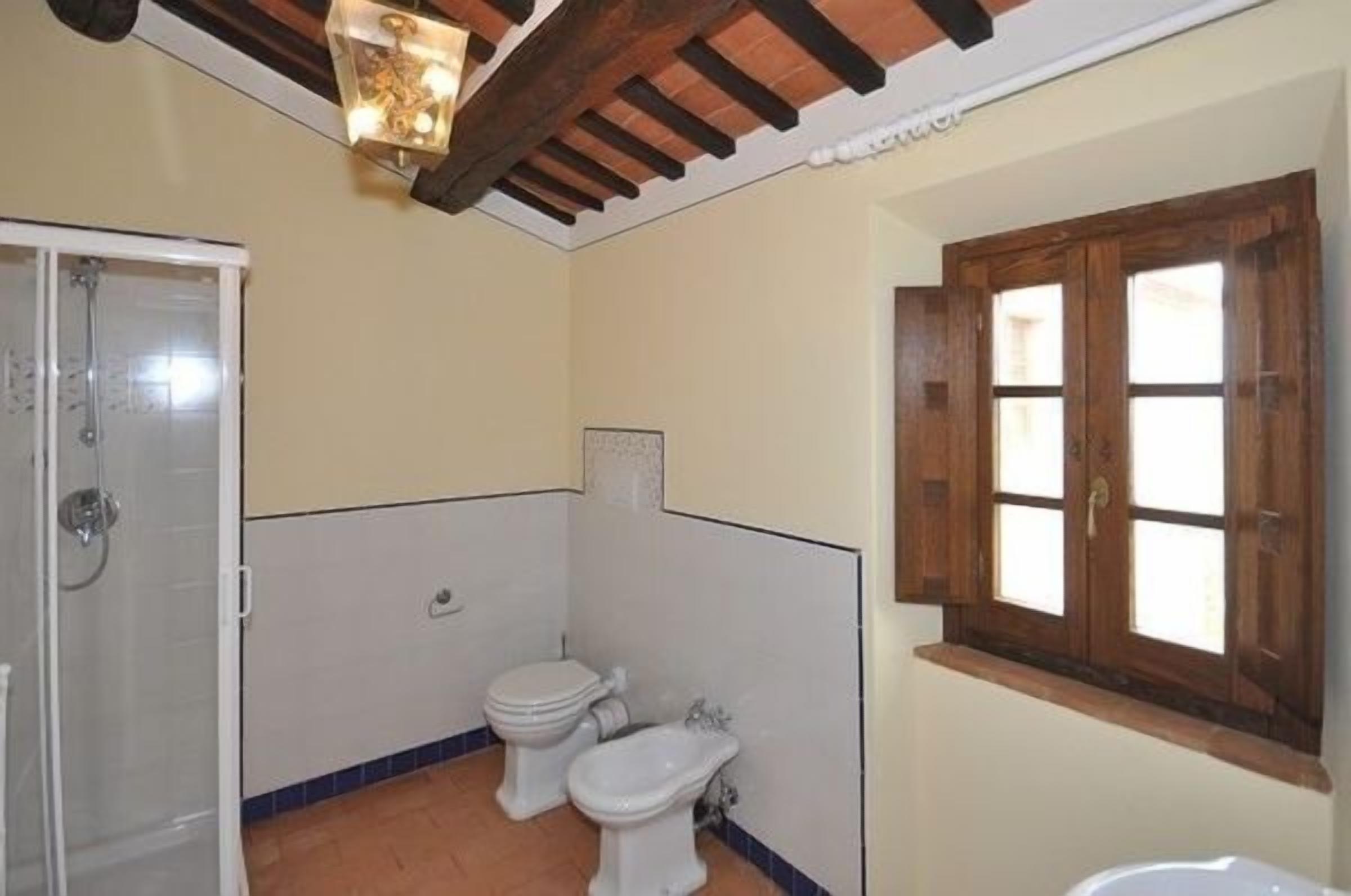 Ein Badezimmer mit Dusche, Toilette, Bidet und einem Fenster mit Holzläden.