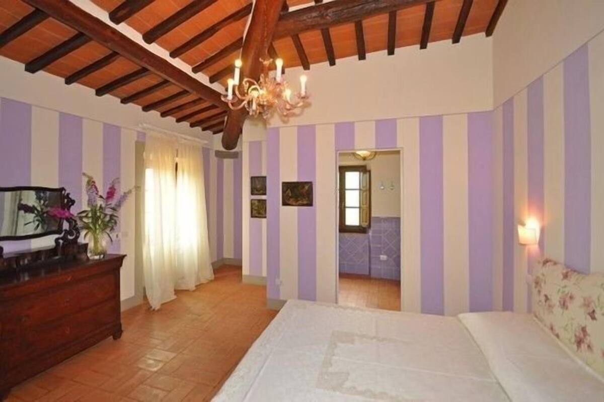A bedroom with striped walls, a wooden ceiling, a bed, a dresser, and a chandelier.