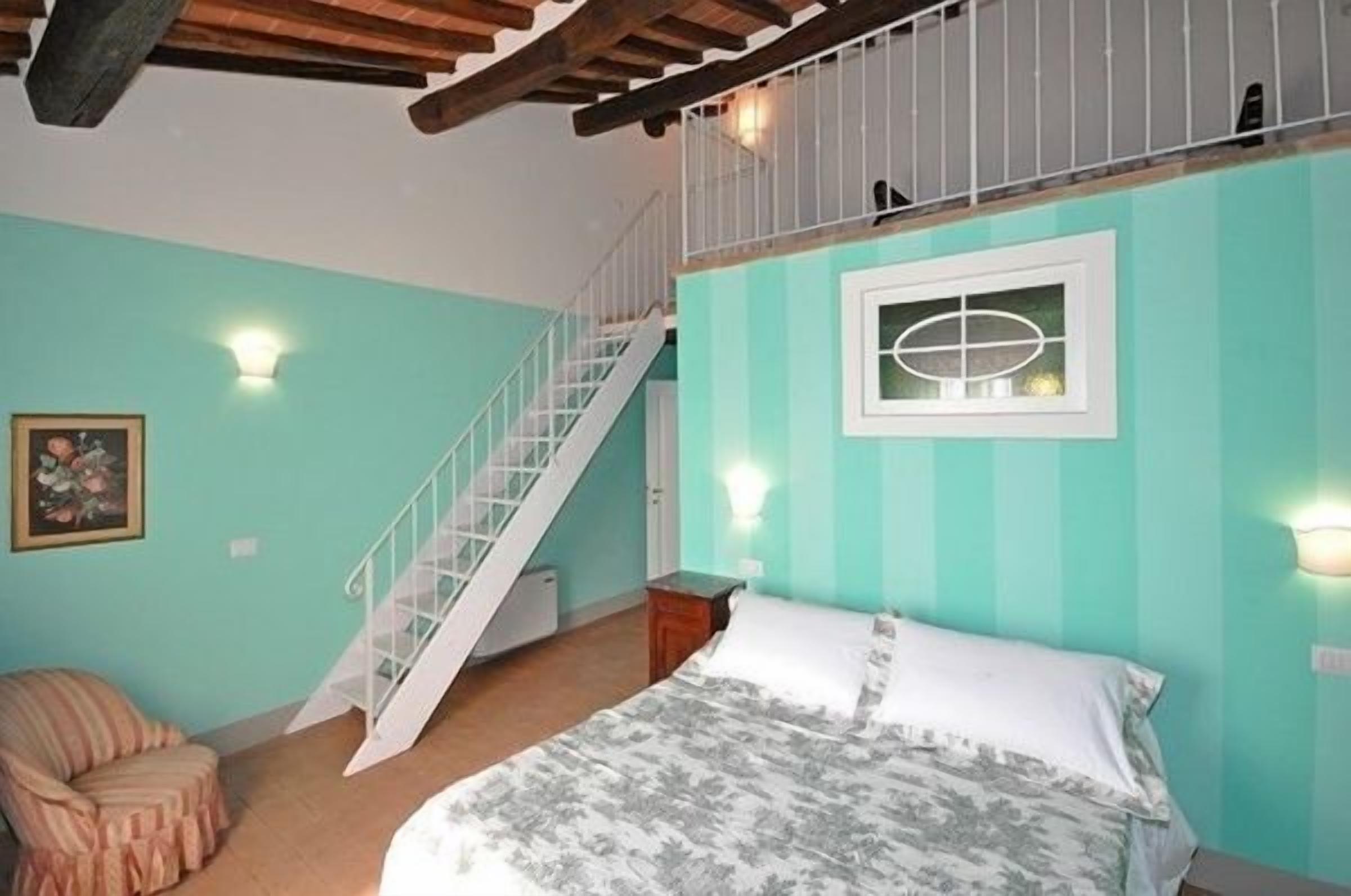 Une chambre à coucher comprenant un lit, une chaise, un escalier et un luminaire fixé au mur.