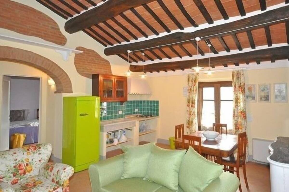 A cozy living room with a green sofa, a dining table with chairs, and a kitchen area with a green refrigerator.