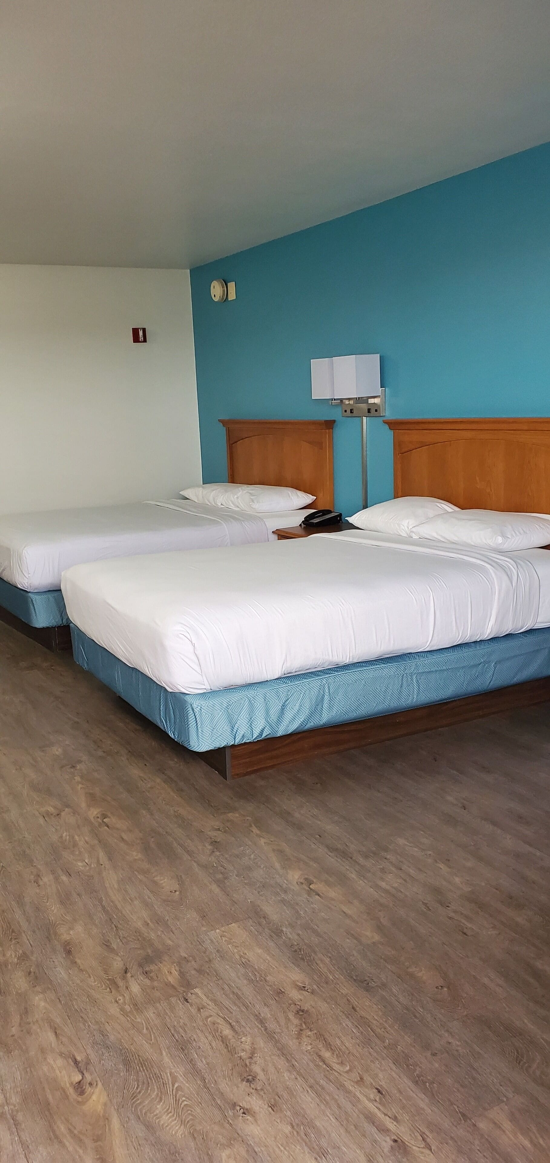 A hotel room with two beds, wooden headboards, a bedside lamp, and a wooden floor.