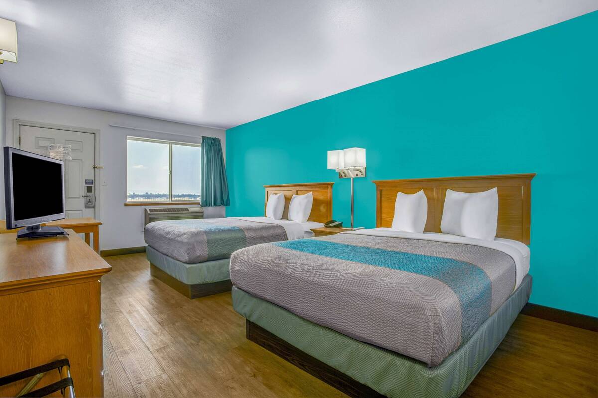 A hotel room with two beds, a desk, a television, and a window with curtains.