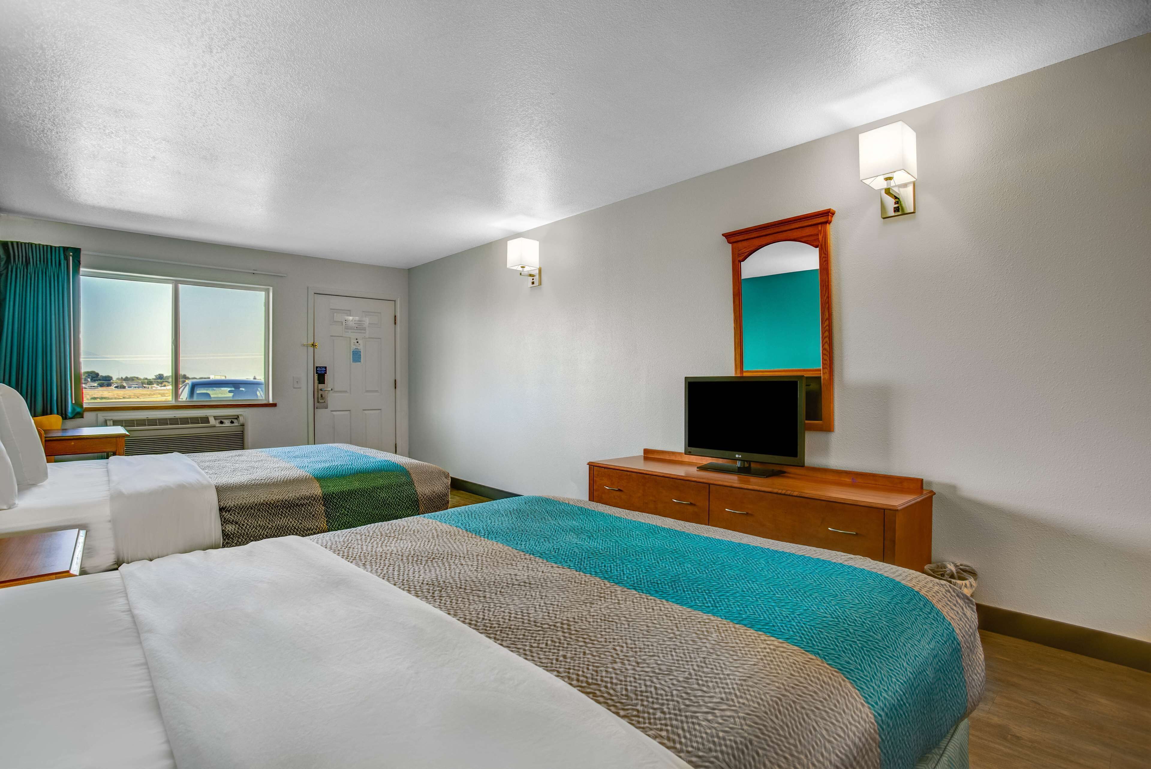A hotel room with two beds, a television, a wooden dresser, a mirror, and a window with curtains.