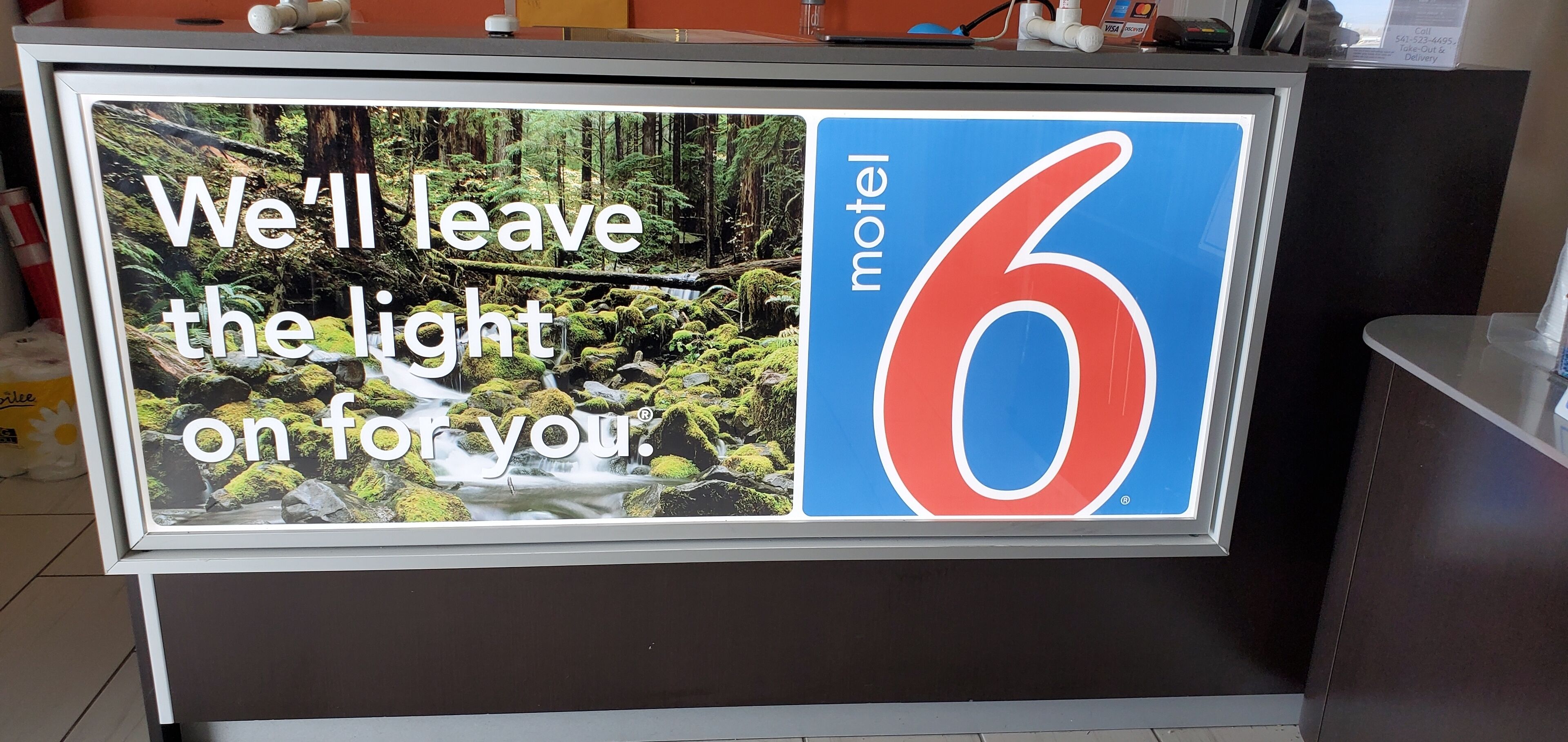 A motel sign with a forest scene and the text "We'll leave the light on for you."