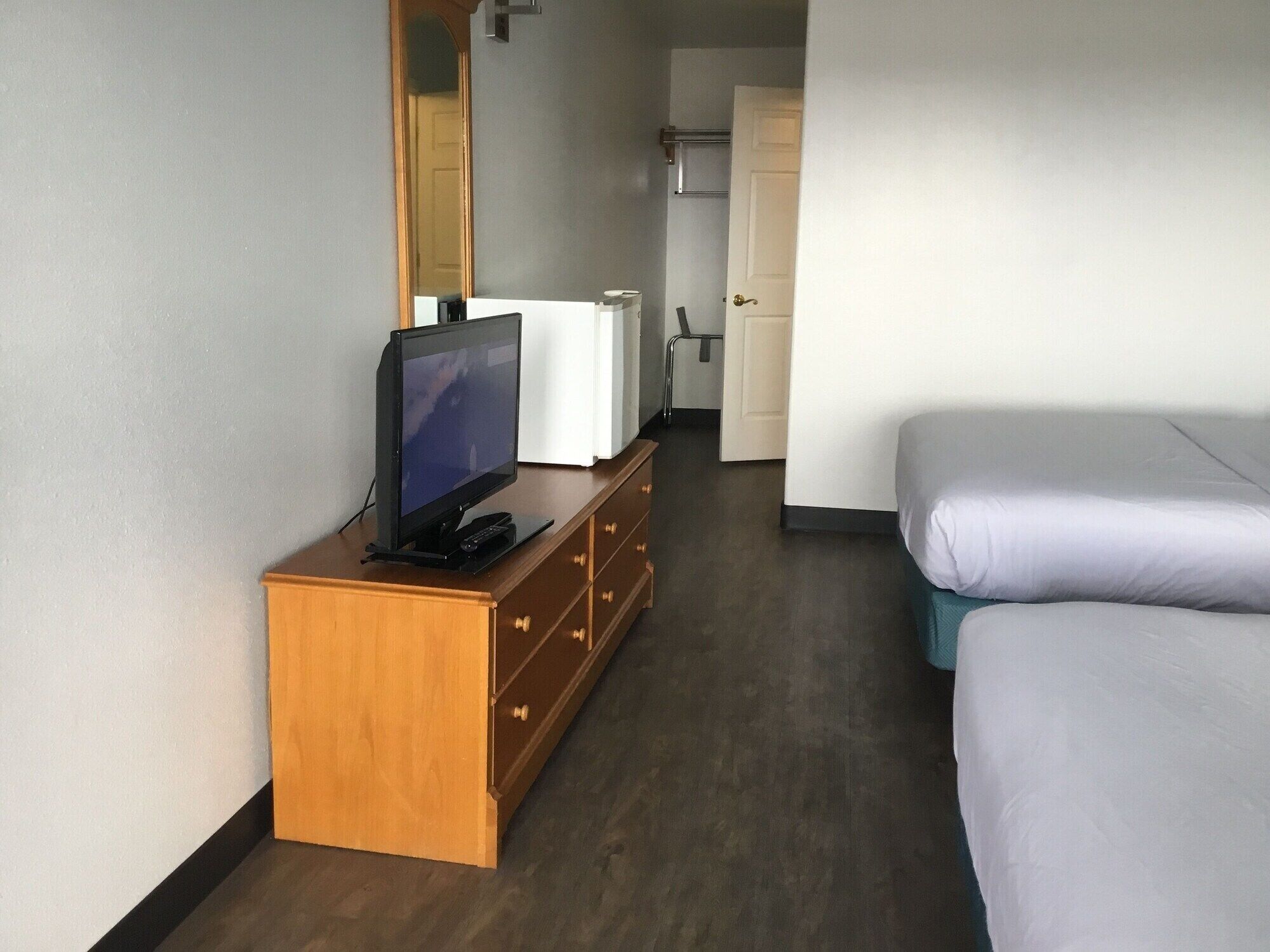 Une chambre d’hôtel avec une commode en bois, une télévision, un lit et une porte donnant sur une autre pièce.