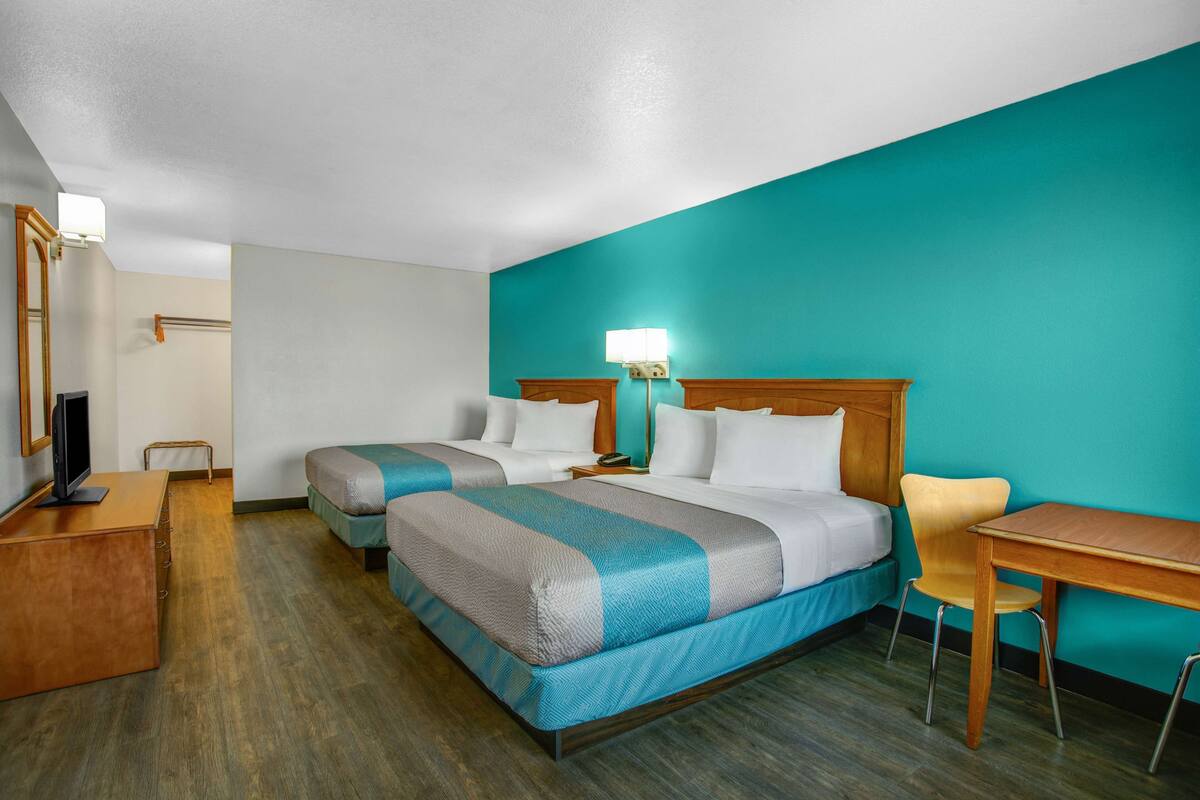 A hotel room with two beds, a desk, a chair, a TV, and a lamp.
