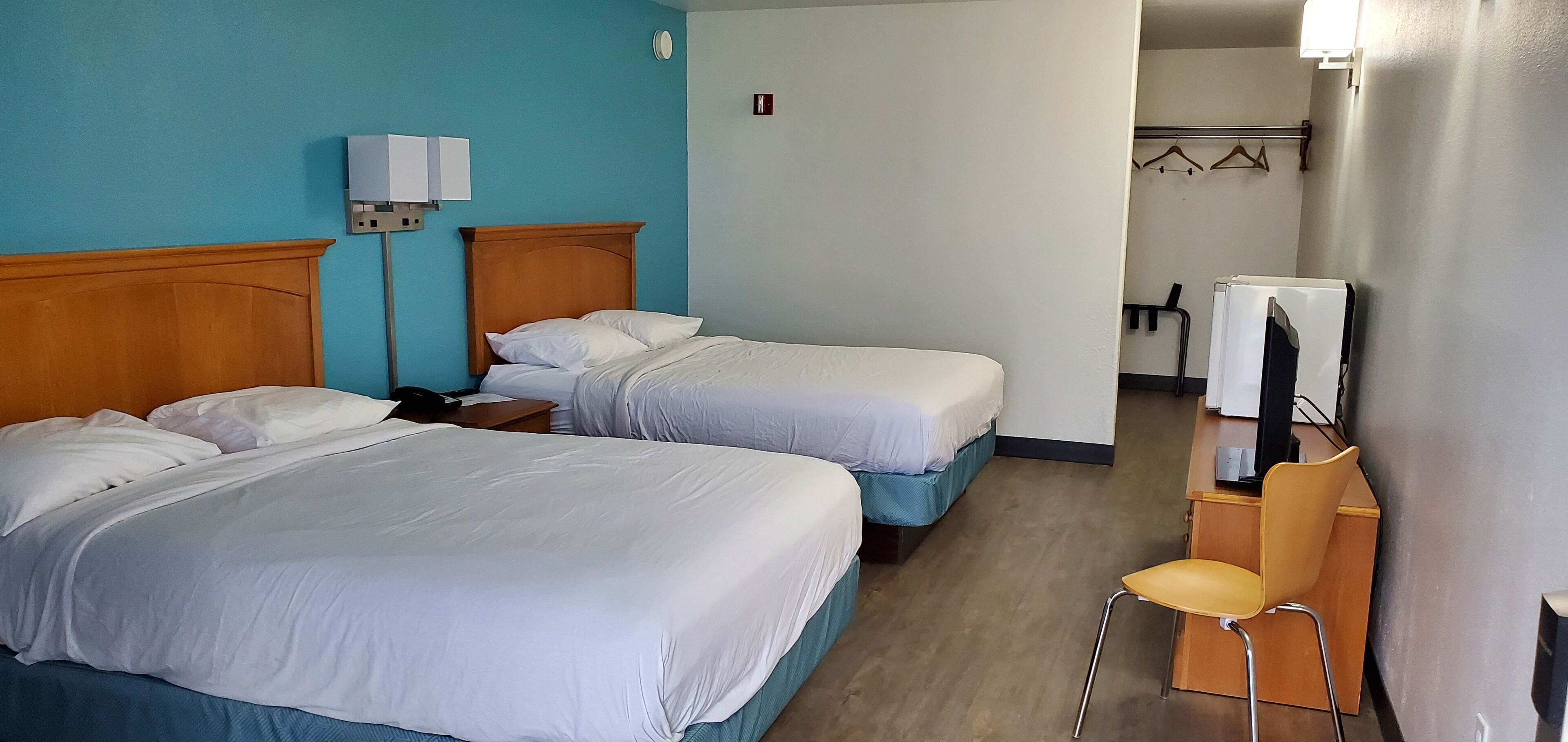 Et hotelværelse med to senge, et skrivebord med en computer, en stol og et fjernsyn.