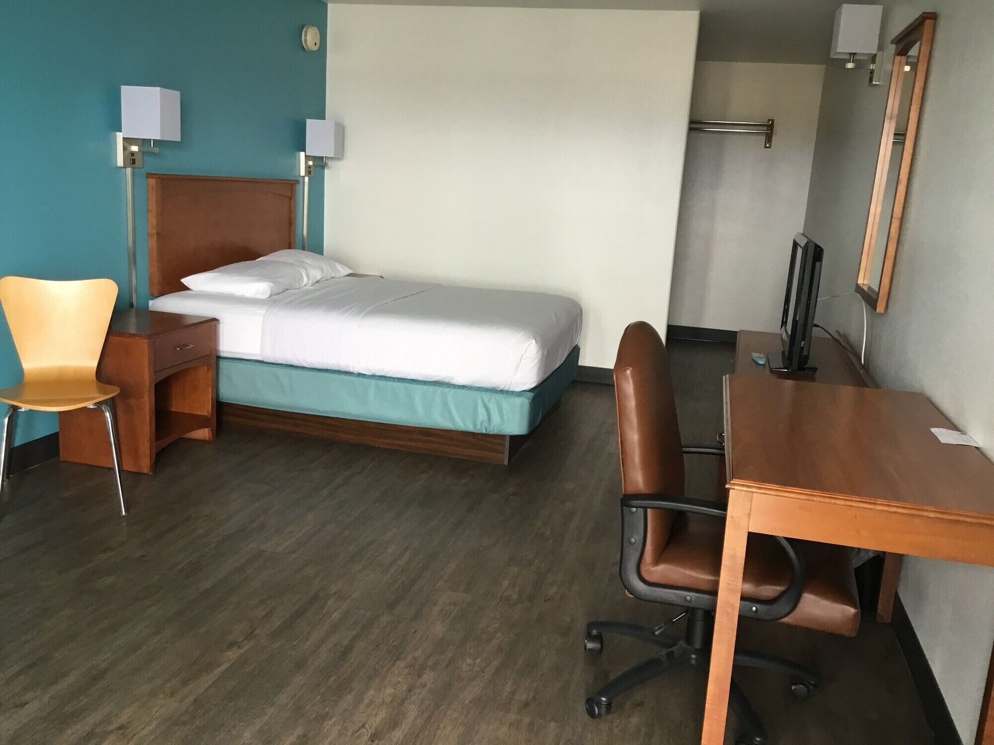 Hotellihuone, jossa on sänky, työpöytä, tuoli, yöpöytä ja lamppu.