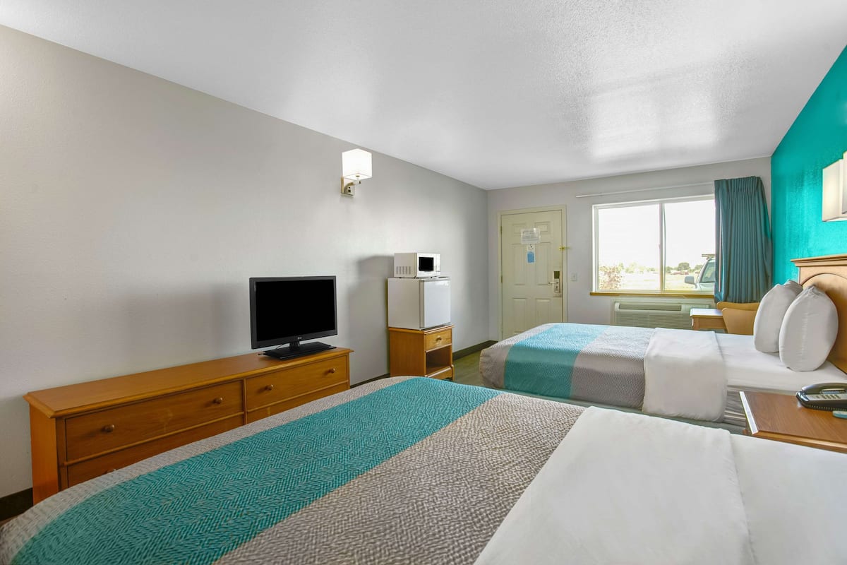 A hotel room with two beds, a television, a microwave, a desk, and a window with curtains.