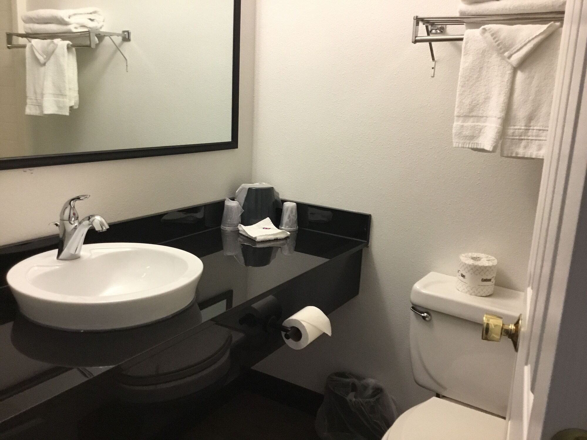 A bathroom with a white sink, black countertop, and a toilet. There are towels hanging on a rack and a trash bin on the floor.
