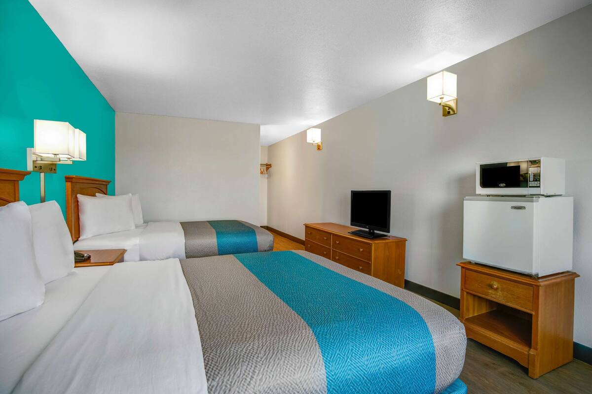 A hotel room with two beds, a television, a refrigerator, and a wooden nightstand.