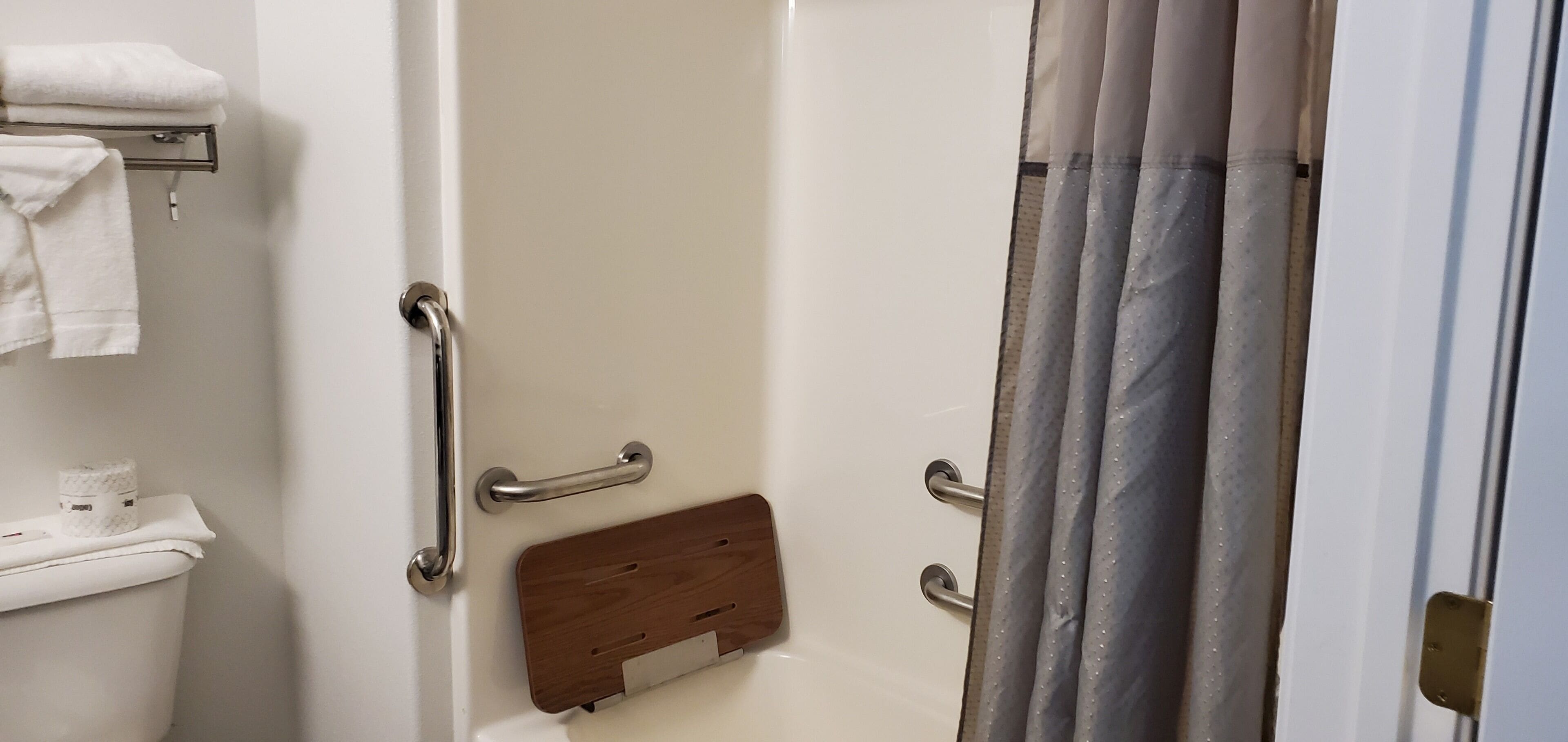 Un baño con un inodoro blanco, un perchero con toallas, una bandeja de madera y una cortina de ducha.