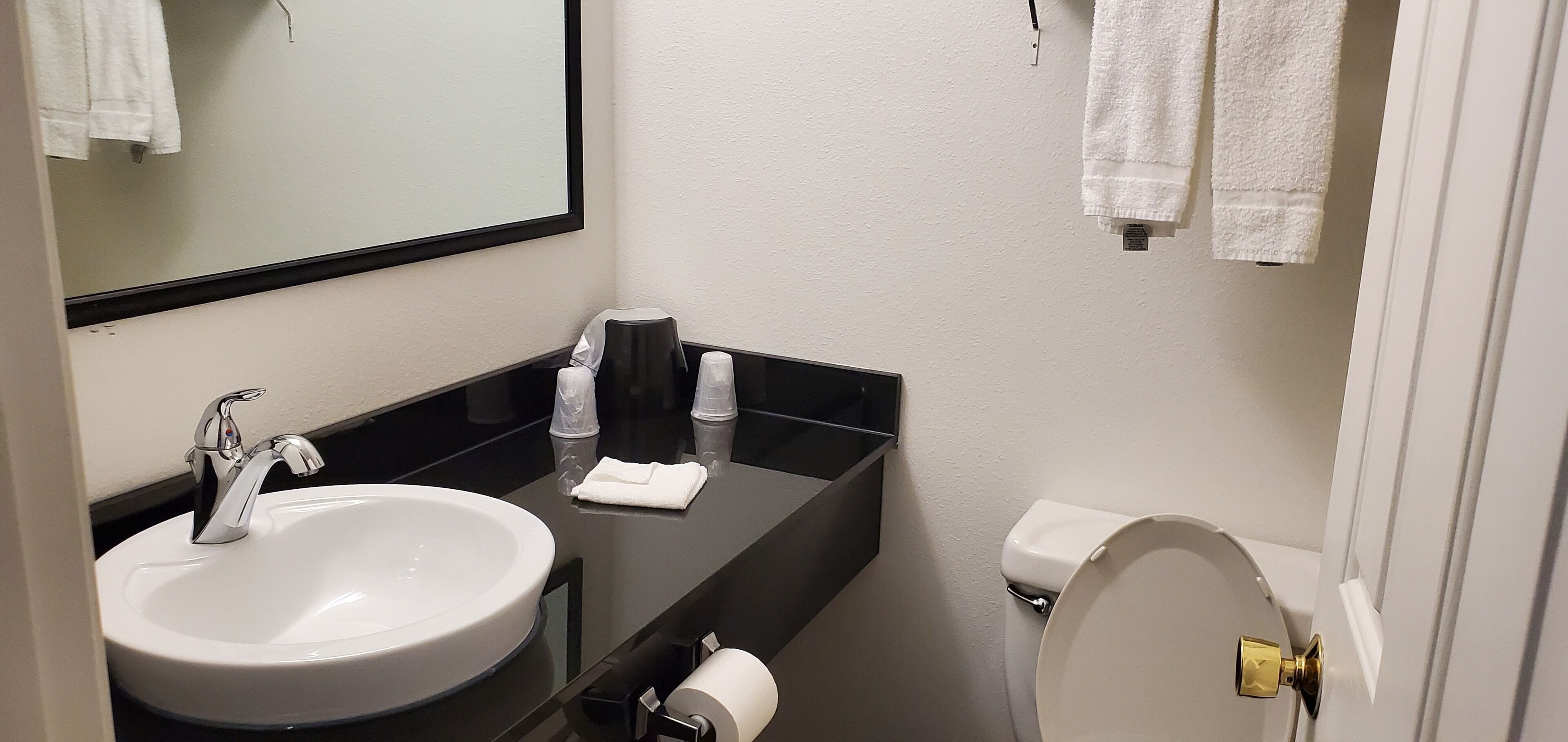 Un baño con lavamanos blanco, encimera negra y un inodoro con detalles dorados.