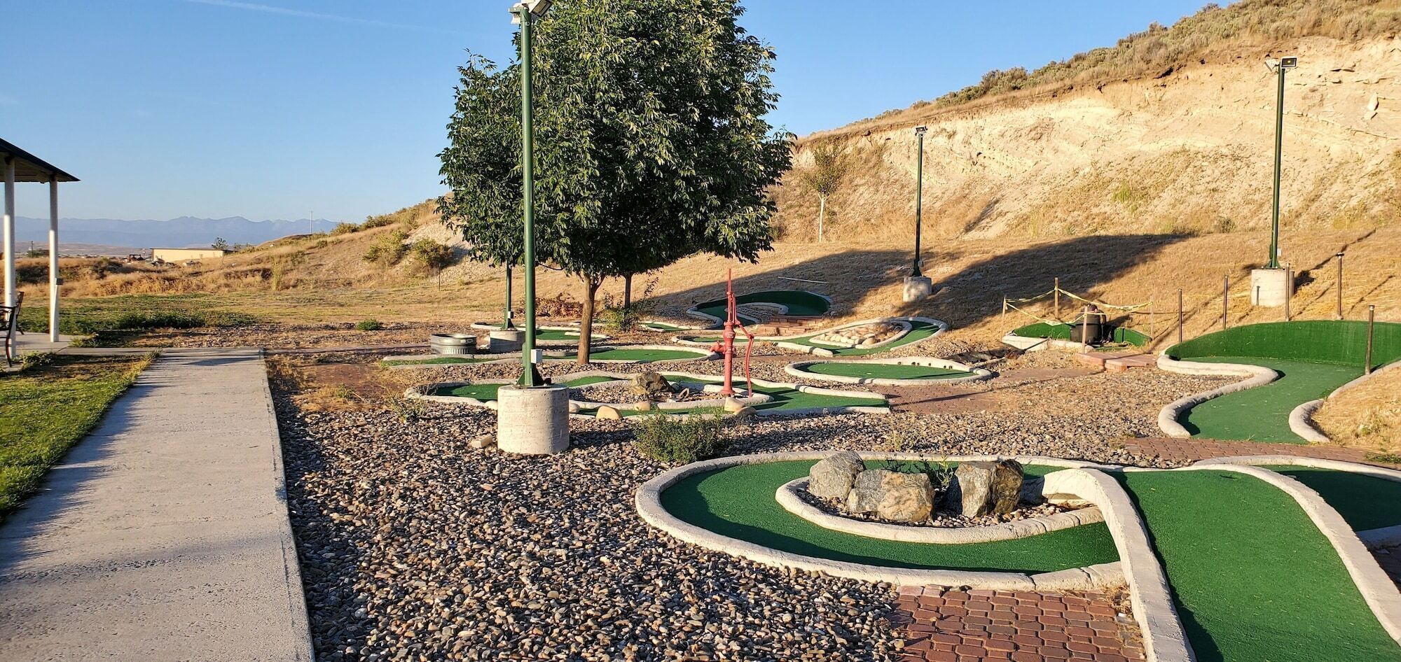 Un campo de golf con un sendero pavimentado, extensas zonas verdes y un paisaje ondulado al fondo.