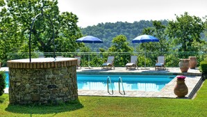 A swimming pool with stone walls, surrounded by grass, and shaded by umbrellas. - Col Di Forche (Monterchi)
