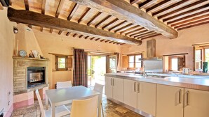 A kitchen with a stone fireplace, white cabinets, and a large window. - Col Di Forche (Monterchi)