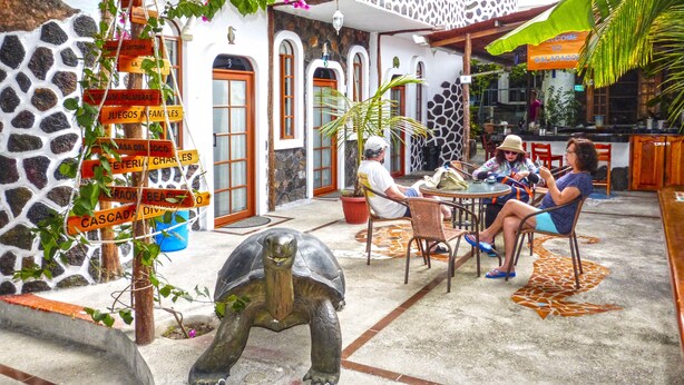 A courtyard with a tortoise statue, outdoor seating, and a sign with multiple directions. - Hotel Coloma Galapagos (Puerto Ayora)