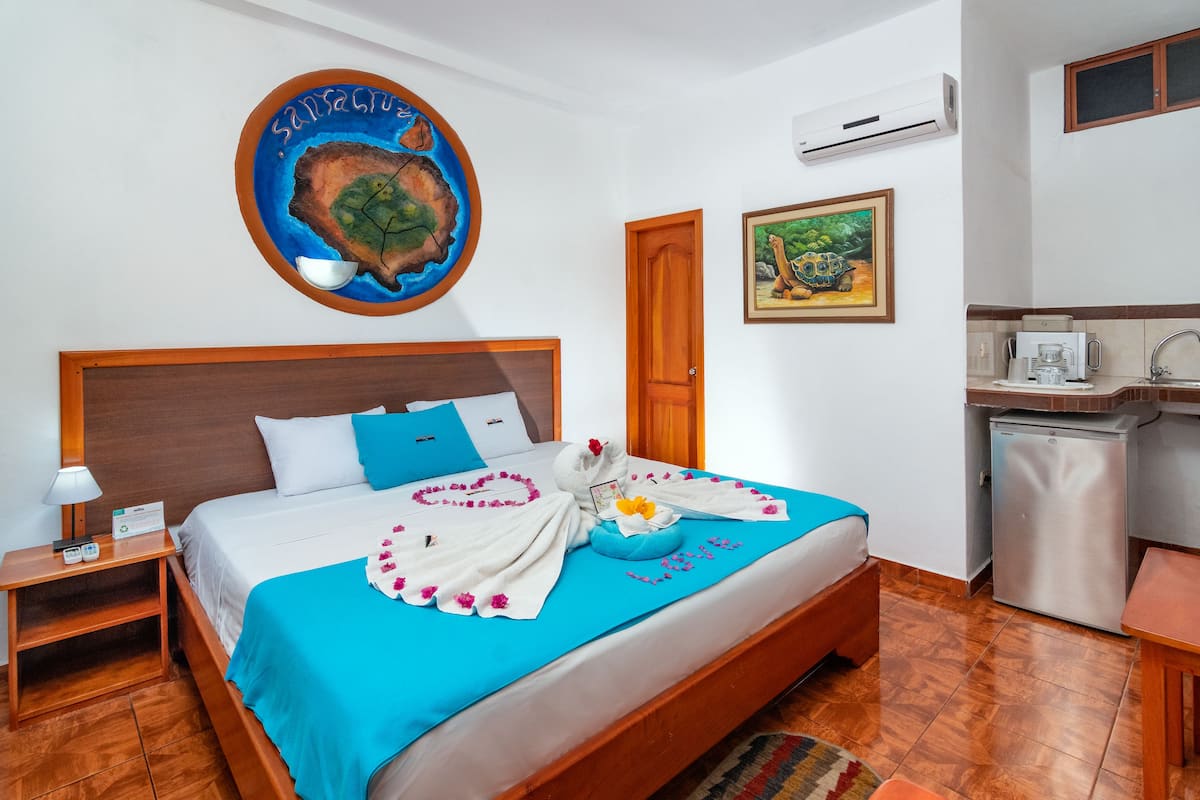 A hotel room with a bed, a nightstand, a desk, a kitchenette, and a bathroom.