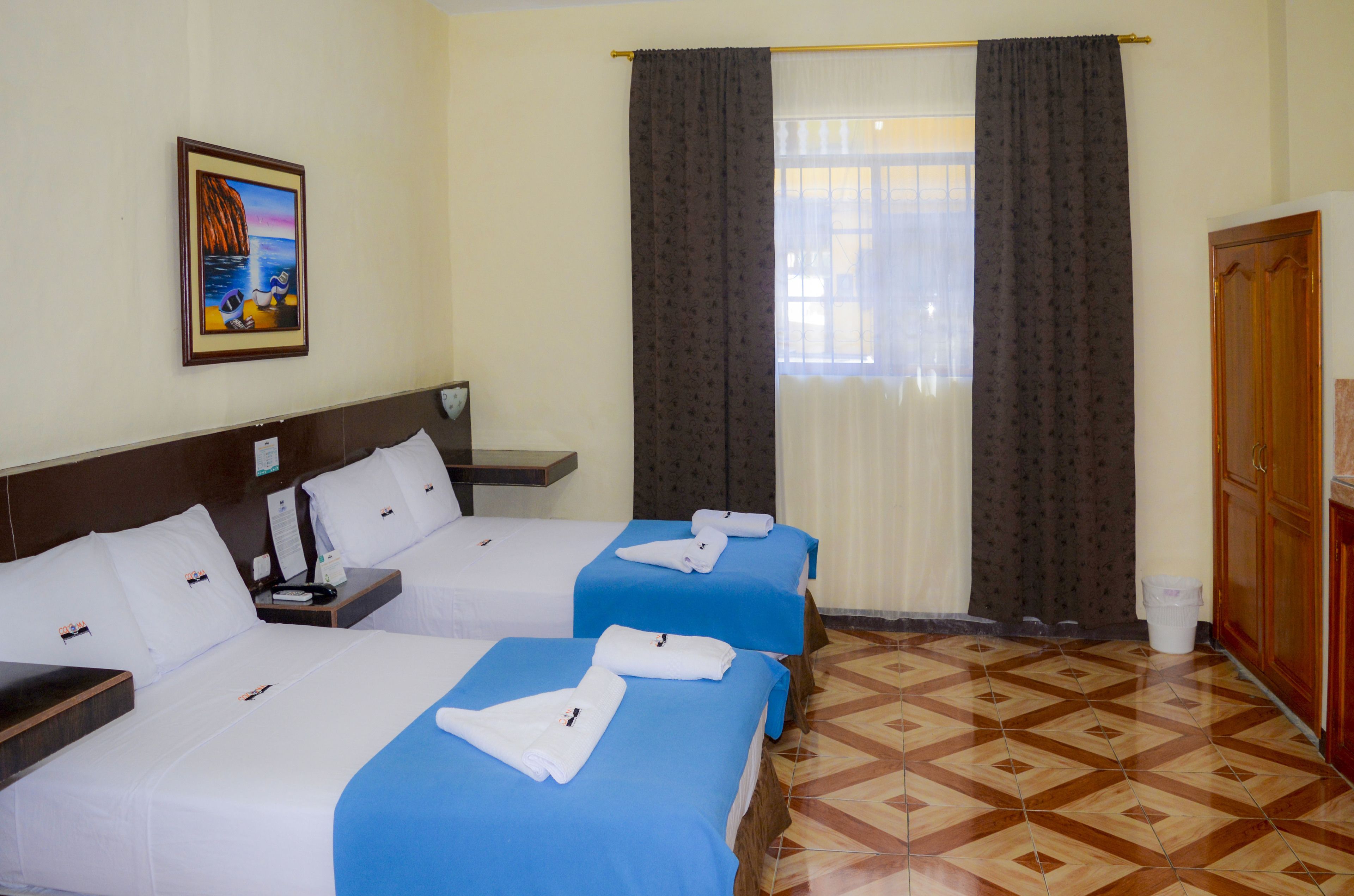 Habitación de hotel con dos camas, un cuadro en la pared, una ventana con cortinas y suelo de baldosas.