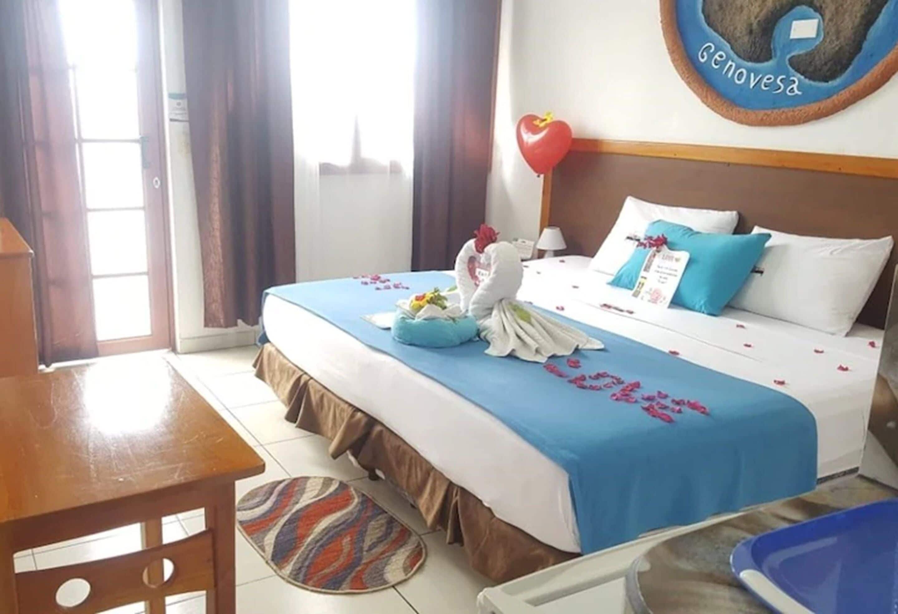 A hotel room with a bed, a desk, a chair, a wall clock, and a window with curtains.