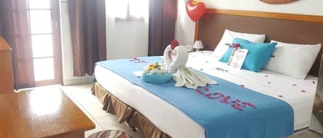 A hotel room with a bed, a desk, a chair, a wall clock, and a window with curtains.