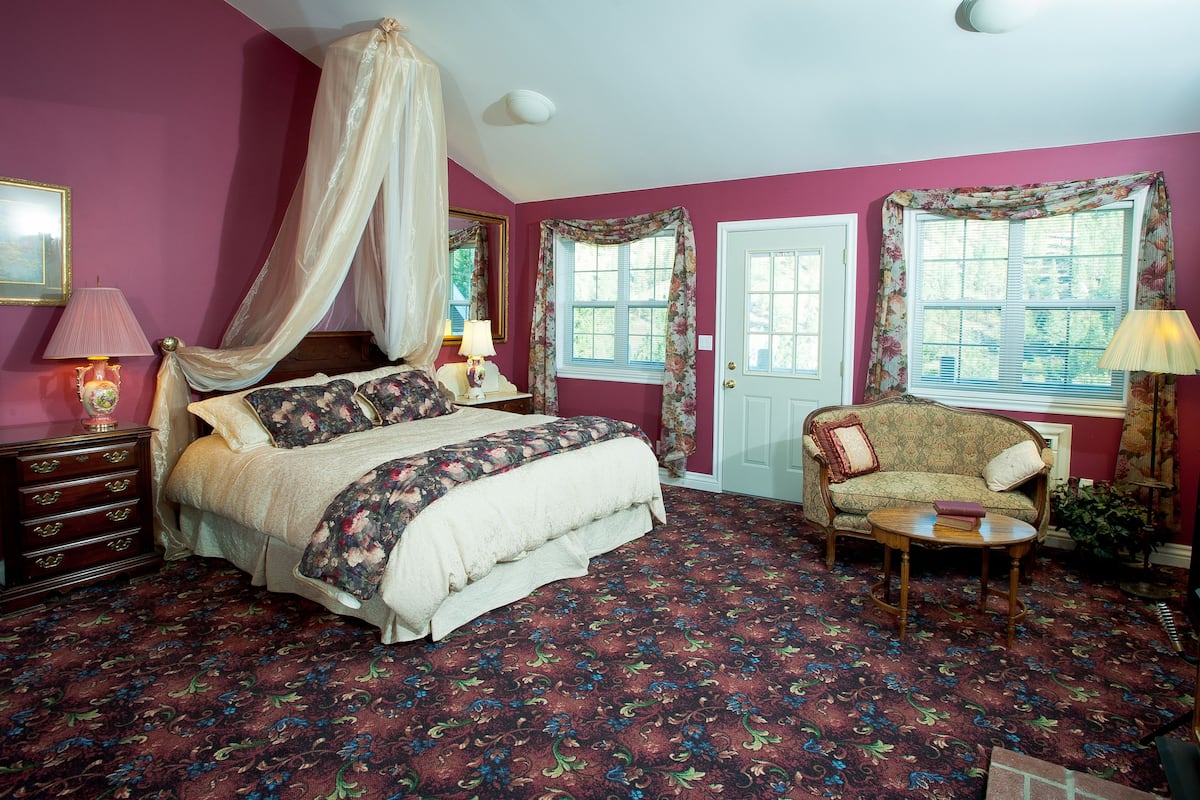 A bedroom with a four-poster bed, a chaise lounge, and a floral-patterned carpet.