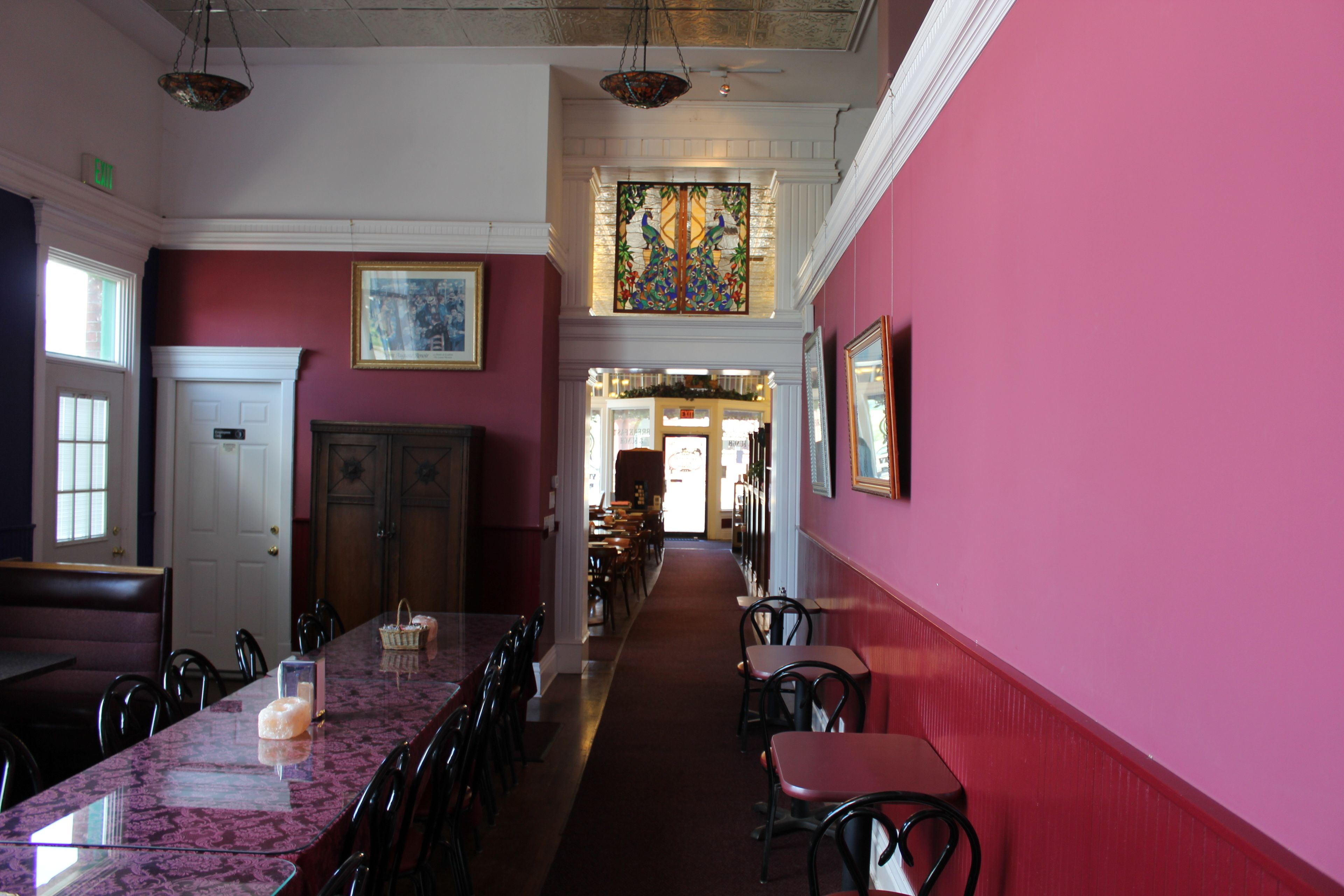 Ein Restaurant mit einer langen Theke, mehreren Tischen und Stühlen. Am Ende der Theke befindet sich eine Tür und eine Treppe, die zu einer oberen Ebene führt.