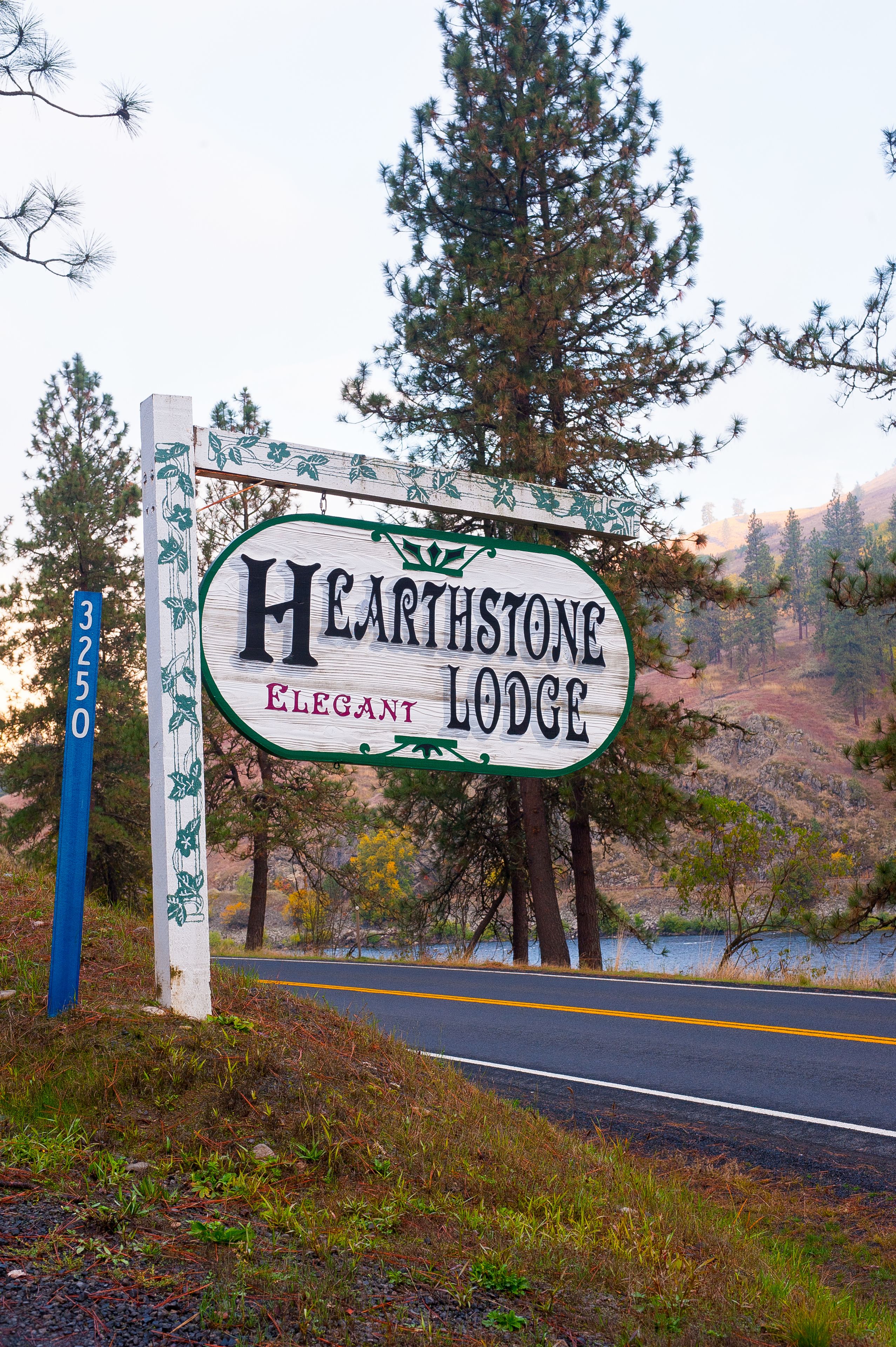A sign for Hearthstone Elegant Lodge with a road and trees in the background.